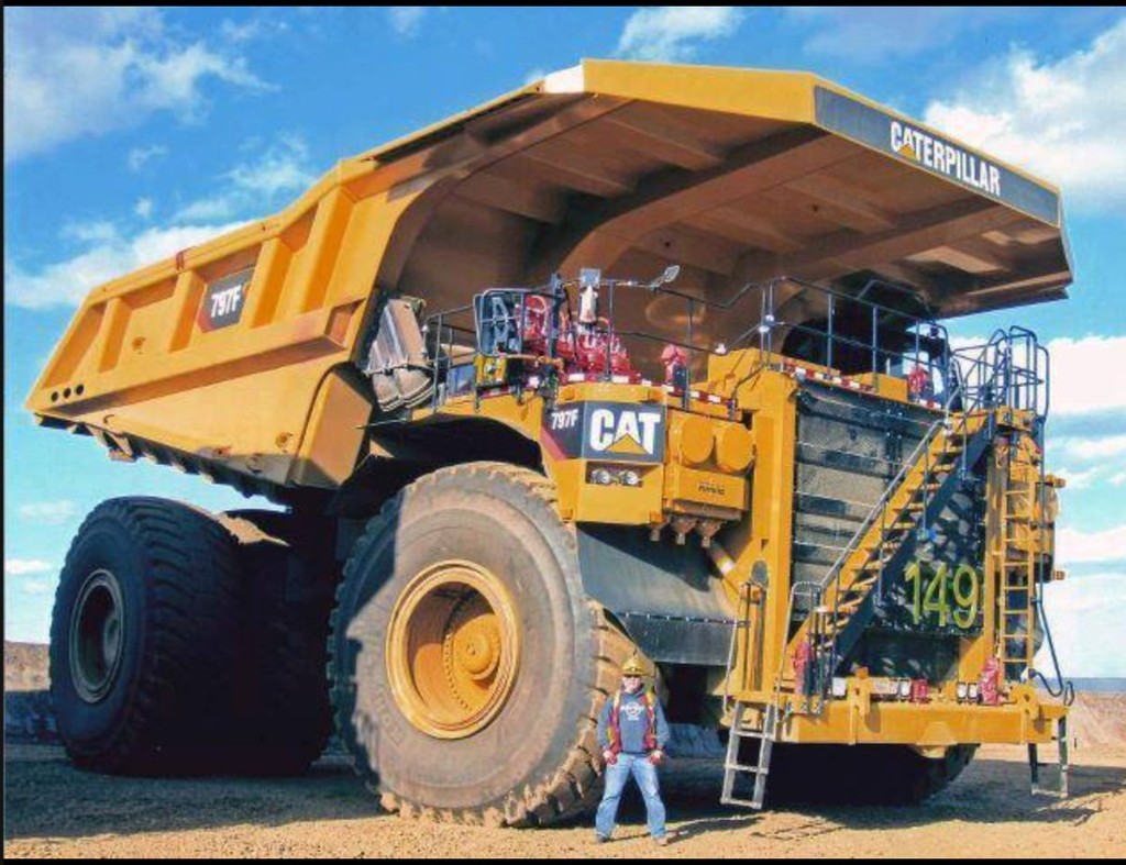 Yellow Caterpillar 797F mining haul truck with a worker beside the tire for scale