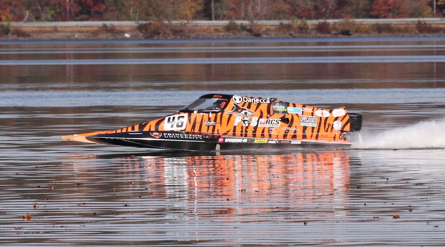 Orange electric hydroplane racing boat skimming across calm water with spray