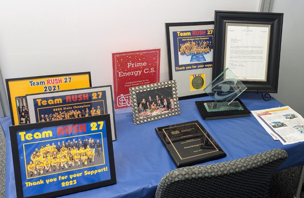 Framed Team RUSH 27 photos from 2021–2024, championship trophies, and sponsor recognition on a table in Troy.